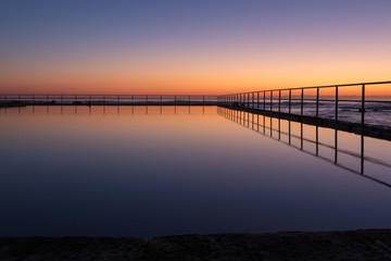 Fototapeta na wymiar Dawn sky reflection in a seaside coastal pool. Early morning, twilight colours.