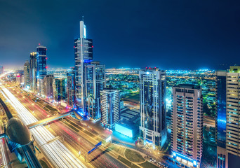 Fototapeta premium Kolorowa panorama dużego, nowoczesnego miasta z oświetlonymi wieżowcami i autostradami. Widok z lotu ptaka na centrum Dubaju, ZEA. Tło podróży i architektury.