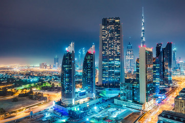Fototapeta premium Spectacular urban skyline with colourful city illuminations. Aerial view on highways and skyscrapers of Dubai, United Arab Emirates.