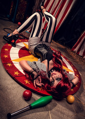 Crazy and beautiful female clown rotates somewhere on scene of dark circus arena
