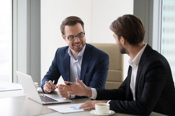 Two smiling businessmen working at laptop in office discussing ideas, happy managers or workers...