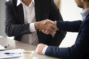 Close up of male colleagues handshake making agreement or closing deal after meeting, business partners shaking hands thanking for successful negotiations, man greeting in office. Partnership concept