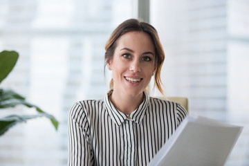 Portrait of smiling millennial businesswoman holding documents looking at camera, headshot of happy woman worker or female ceo posing with paperwork making picture at corporate photoshoot. - obrazy, fototapety, plakaty