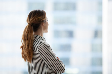 Smiling millennial businesswoman looking in window thinking about future career opportunities,...