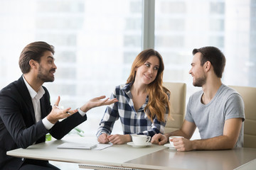 Happy millennial couple look at each other visiting consultant or broker, boyfriend and girlfriend consulting at real estate agent, deciding to make purchase, spouses talk with banker taking loan