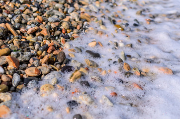 small stones on the beach covered by white wave foam