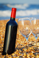Sealed bottle of red wine with two wineglass on the beach close up