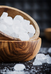 White crystal candy sugar in wooden bowl on black table, selective focus