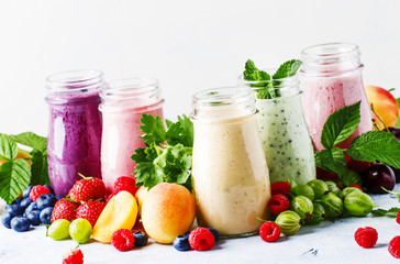 Fototapeta na wymiar Healthy and useful colorful berry cokctalis, smoothies and milkshakes with yogurt, fresh fruit and berries on gray table, selective focus