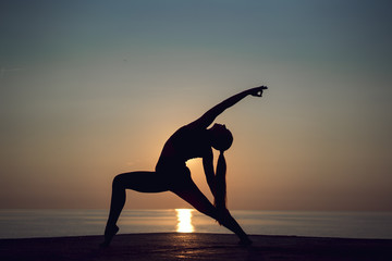 Yoga meditation woman silhouette on the ocean during amazing sunset. Healthy woman balancing and practicing meditation and energy yoga on the pier in morning on the sunrise. Healthy and sport concept