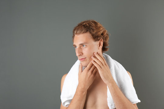 Young man touching his soft skin after shaving on gray background