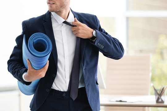 Young handsome businessman holding yoga mat in office. Gym after work
