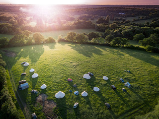 Aerial view of idyllic campsite at sunset with North London countryside as the backdrop. Bell tents and camper vans make up a trendy camping field taken from above by drone.