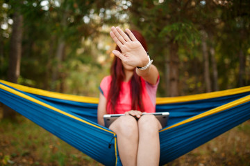 Photo of brunette with laptop with hand outstretched sitting in hammock