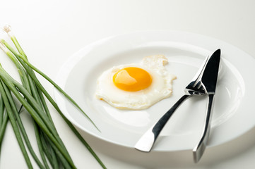 Scrambled eggs on a white plate with a fork and a knife. Green onion near the plate