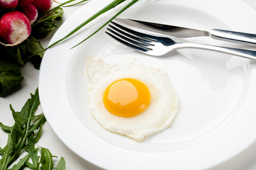 Scrambled eggs on a white plate with a fork and a knife. Green onion near the plate