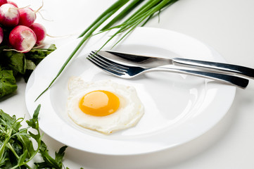 Scrambled eggs on a white plate with a fork and a knife. Green onion near the plate