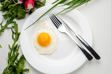 Scrambled eggs on a white plate with a fork and a knife. Green onion near the plate