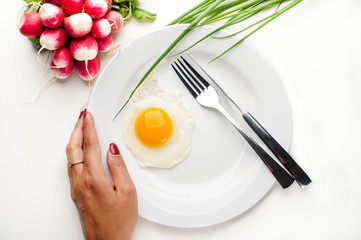 Women's hands hold a white plate with an egg, a fork and a knife