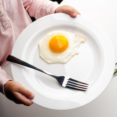 Children's hands hold a white plate with an egg, a fork and a knife.