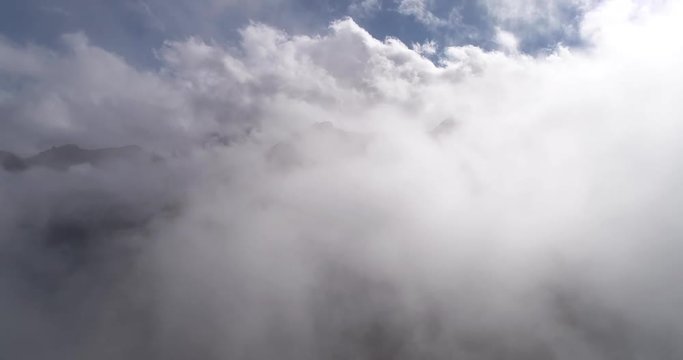 Time lapse. Aerial view of misty foggy mountain top. Drone filming hills summit while clods moving and circling around summit. Clouds hanging low. Mist all over the scene. Austria. Alps