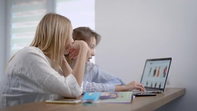 Two girls shopping online at home, choosing clothes on internet site, stylish clothes.