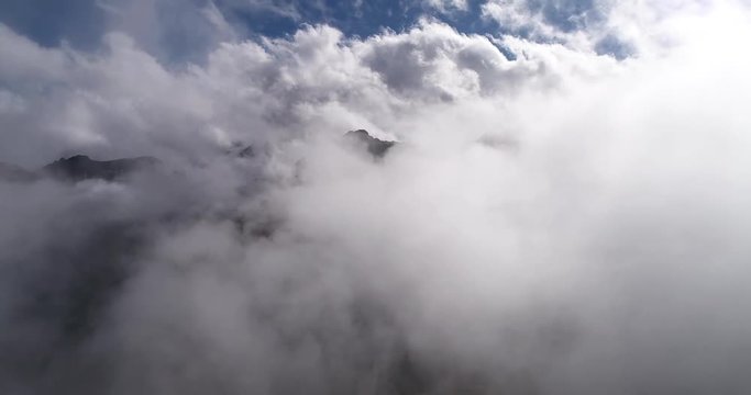 Aerial view of misty foggy mountain top. Drone filming hills summit while clods circling around summit. Clouds hanging low. Mist all over the scene. Austria. Alps