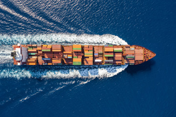 Top down Ansicht auf ein beladenes Containerschiff in voller Fahrt über blauem Meer - obrazy, fototapety, plakaty
