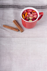 Чай с фруктами в красной чашке на льняной скатерти крупным планом. Палочки корицы 