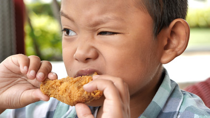 Cute asian boy are happy eating fried chicken leg in restaurant