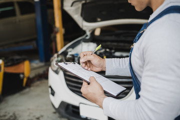 Hand of young man mechanic holding clipboard checklist the car at service center repair