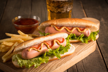 Photo of barbecue grilled hot dog with yellow mustard and ketchup on wooden background. Hot dog sandwich with potato fries and sauces.