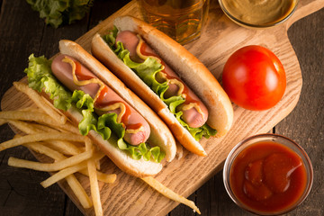 Photo of barbecue grilled hot dog with yellow mustard and ketchup on wooden background. Hot dog sandwich with potato fries and sauces.