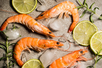 Tiger shrimps with lime, lemon, rosemary and black pepper spices on stone background. Fresh tasty prawns ready to be cooked.
