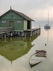 Fototapeta na wymiar Grünes Bootshaus mit untergegangenem Ruderboot am Ammersee