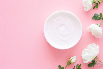 Opened white jar of natural herbal cream for women on pastel pink table. Beautiful white roses. Fresh flowers. Care about clean and soft face, hands, legs and body skin. Empty place for text.