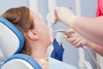 Patient visiting a dentist office. Adult woman sitting in chair. Dental hygienist's hands in rubber protective gloves working with tools.