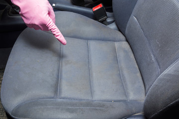 Man's hand in rubber protective glove with finger pointing to dirty textile driver's seat. Car's interior problem and solution. Cleaning concept.