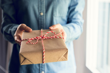 Giving a gift, Woman hands holding handmade present wrapped in brown paper. Christmas time, light and shadow.