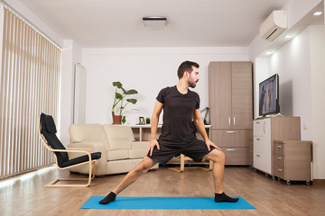 Bearded man doing Warrior II yoga posing and stretching his muscles. Physical health.