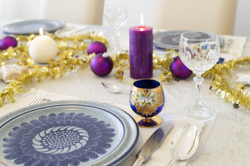 Close-up of a decorated dining table with burning candles, sterling cutlery, crystal glasses, colorful christmas balls and gold tinsel