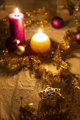 Christmas decoration details on a dining table. Burning candles, christmas balls, stars and gold tinsel