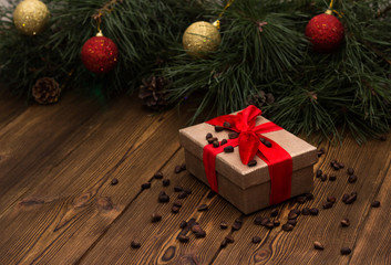 Fototapeta na wymiar A box with a Christmas gift tied with a red ribbon and sprinkled with pine nuts on a wooden background, in the background a Christmas tree with Christmas toys, a gift for Christmas and a new year