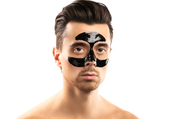 Young guy with a black charcoal mask on his face on white background.