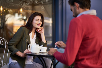 Happy being with you. Charming woman sitting at the table with cup of tea and looking at bearded man with smile