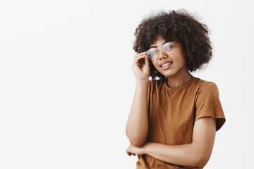 Close-up shot of good-looking stylish modern dark-skinned female touching glasses and gazing with...