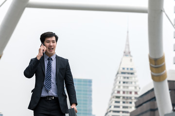 A portrait of Asia young business man walking in the city and using smartphone for talking about jobs and be smile have a happy feeling in the work done and successful. Close deals. Copy space