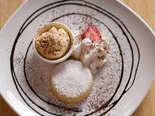 Yellow icecream with white cream and strawberry in white plate closeup top view.