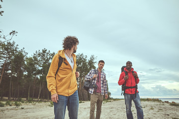 Obraz na płótnie Canvas Outdoor activity. Three buddy having stroll along seashore. They have conversation about their trip