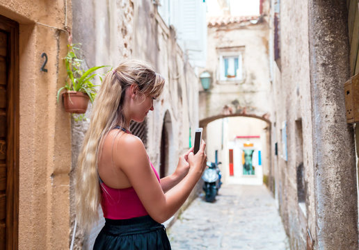 Young tourist woman taking photo using mobile phone on old narrow street in Croatia, travel lifestyle